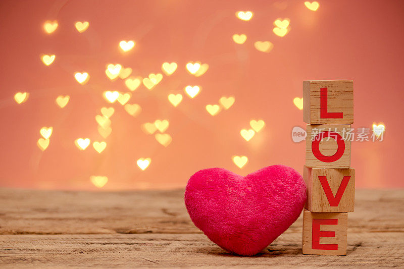 wooden cube with red text love and small pink fluffy heart place beside on wooden table with copy space, defocus heart shape bokeh light sparkling decorate for Valentine's day background
